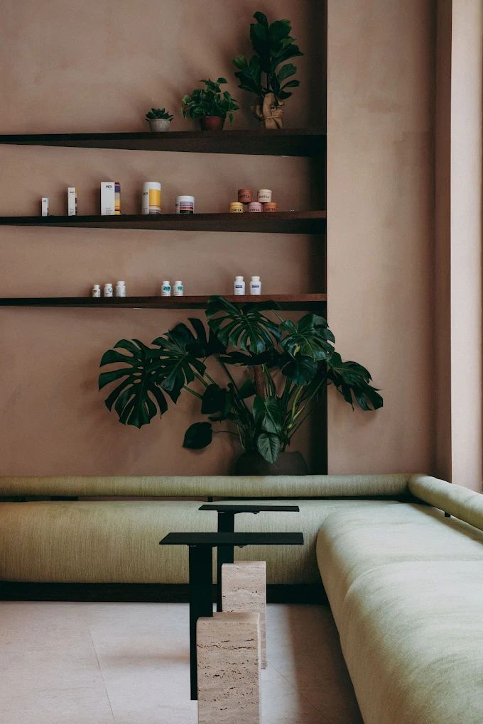 A warmly decorated, contemporary sauna hub with creamy and terracotta plaster walls, curvilinear upholstered furniture with green fabric, wooden details, and warm pendant as well as spherical sconce lighting throughout.