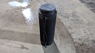 Tronsmart T7 portable Bluetooth speaker outdoors in the rain on a concrete pavement