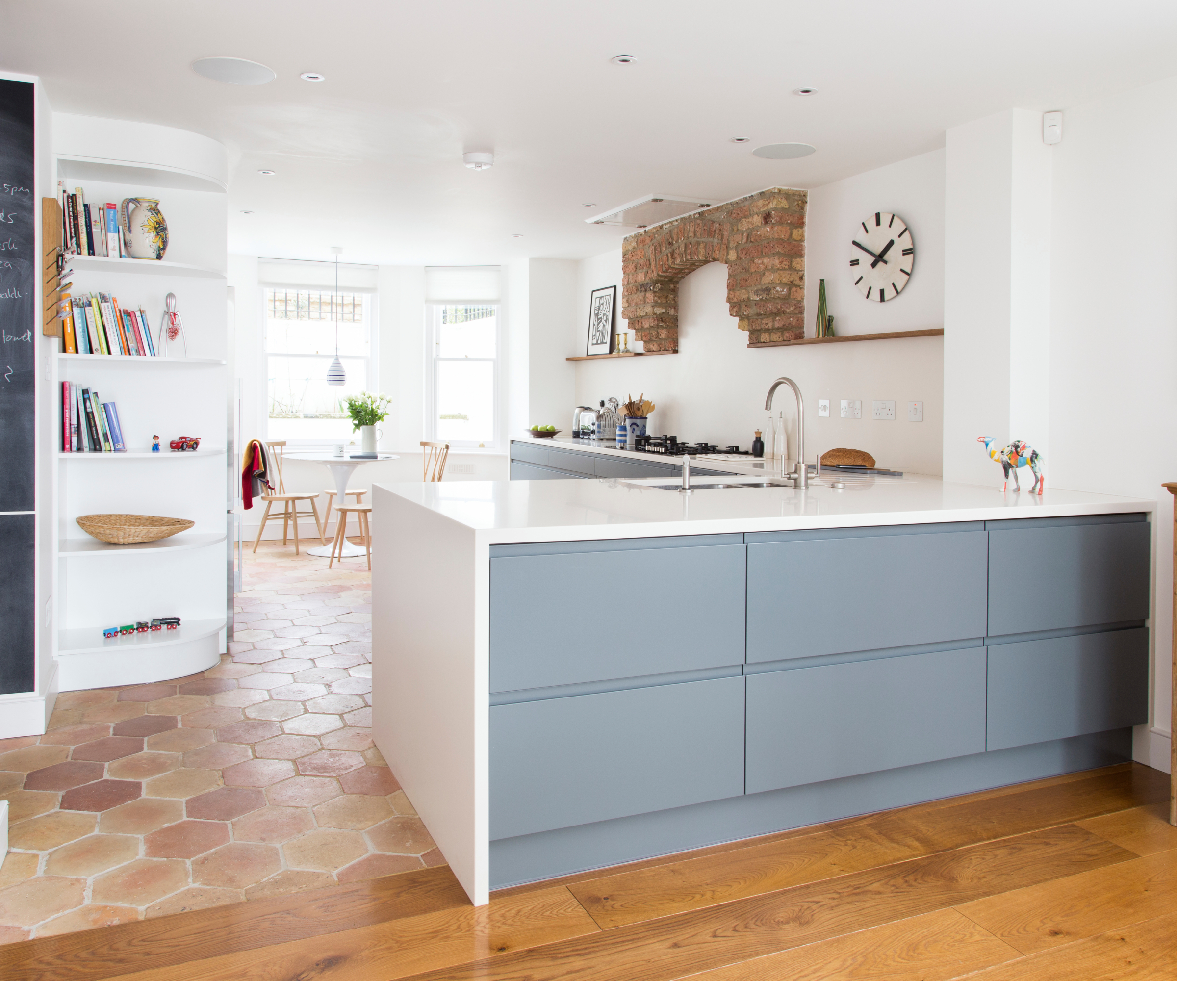kitchen island with blue drawers, white waterfall worktop, wooden flooring on one side and tiled on the other side