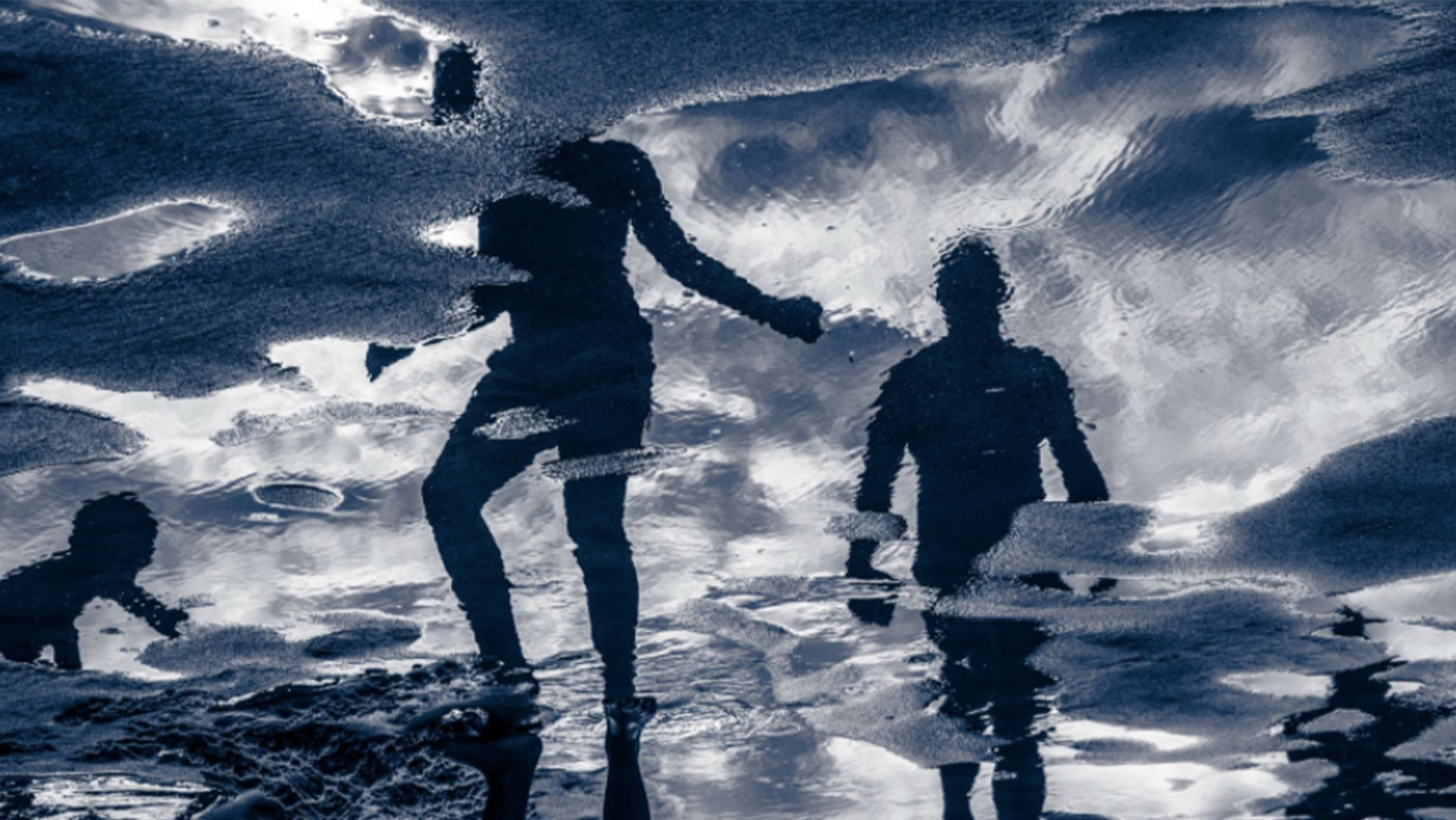 Reflections of people in a puddle on a beach.