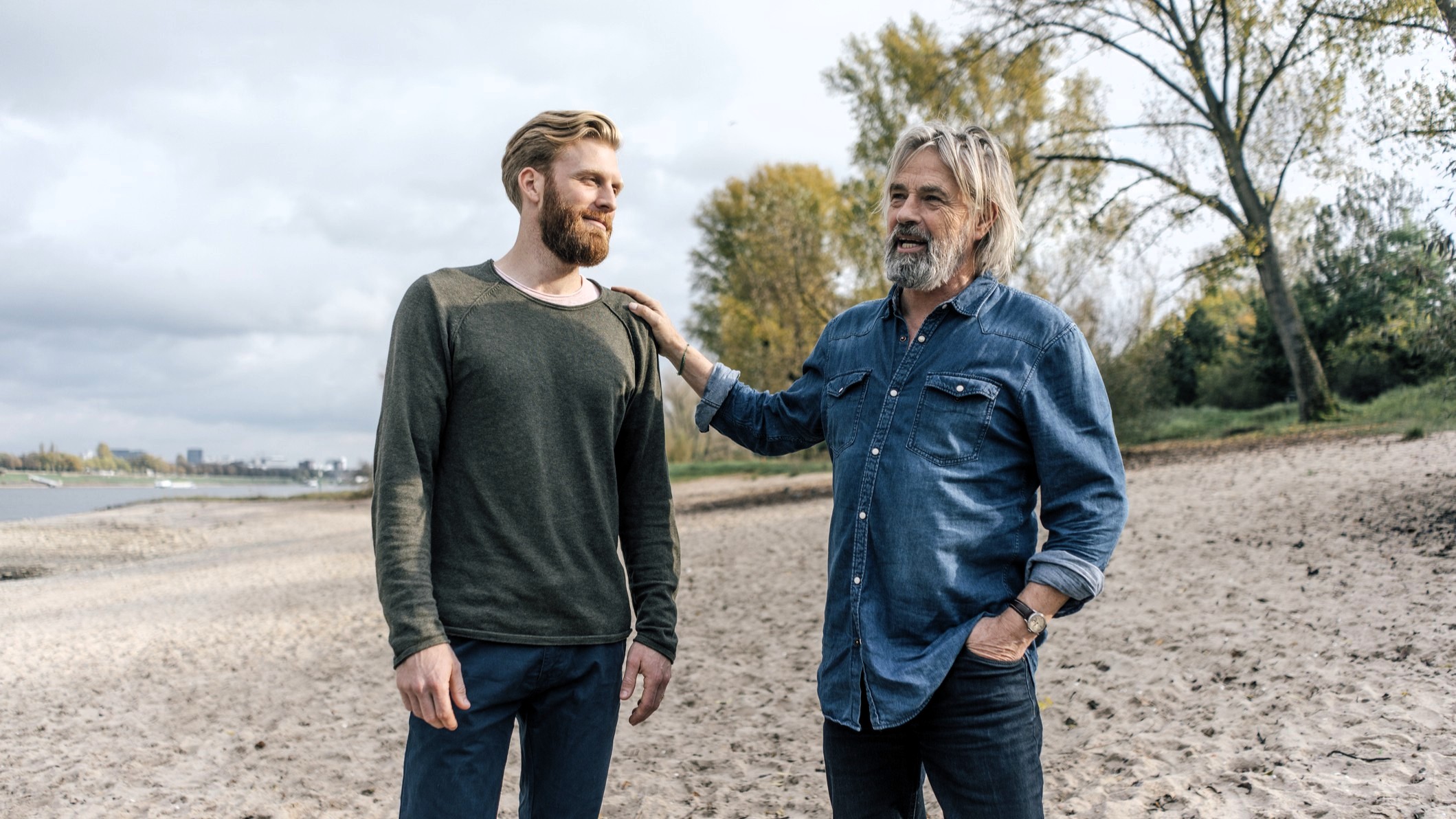 A father and his adult son have a talk on the beach. 