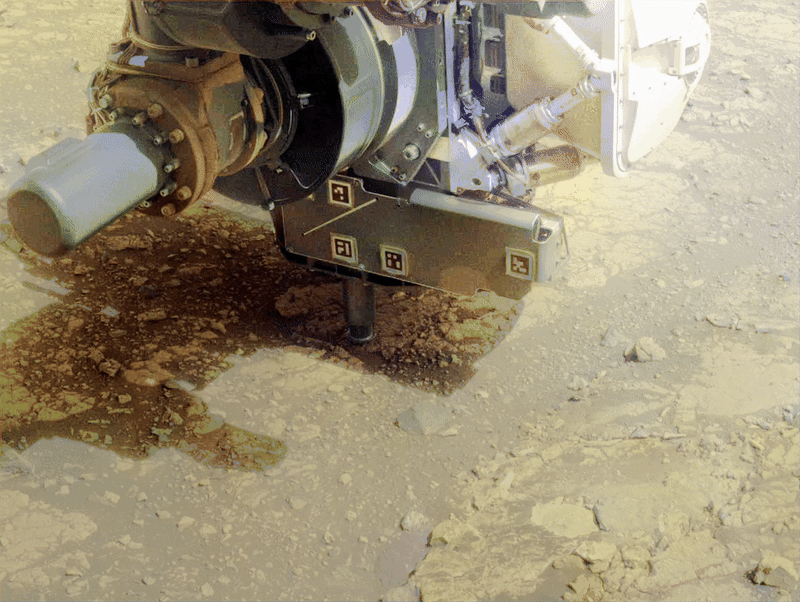 A metal machine uses a drill to dig into reddish-brownish soil