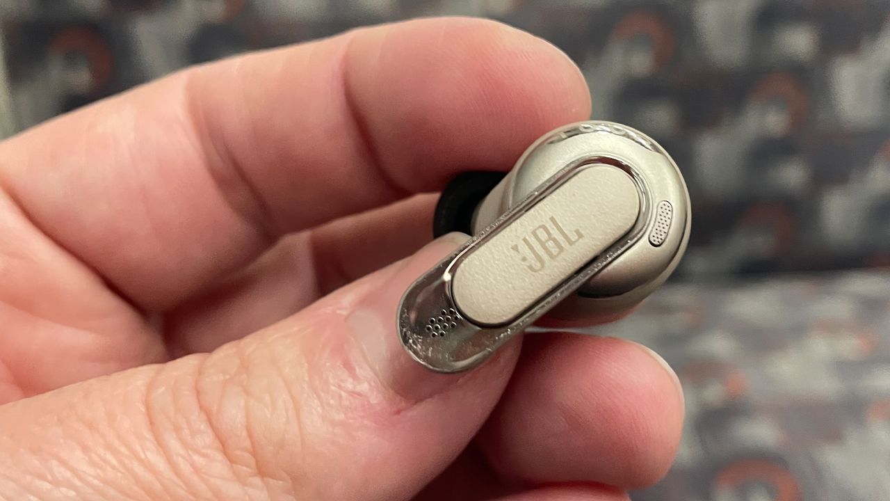 A hand holding a single JBL Tour Pro 3 earbud with the eartip not visible.