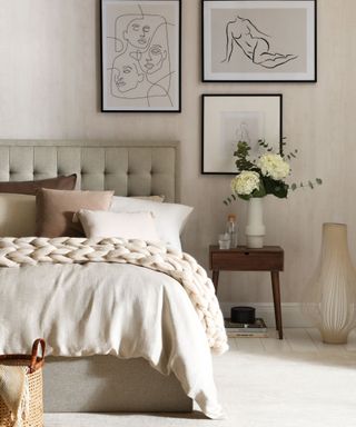 A gray bedroom with a gray bed with brown pillows, black and white wall art, and a nightstand with flowers