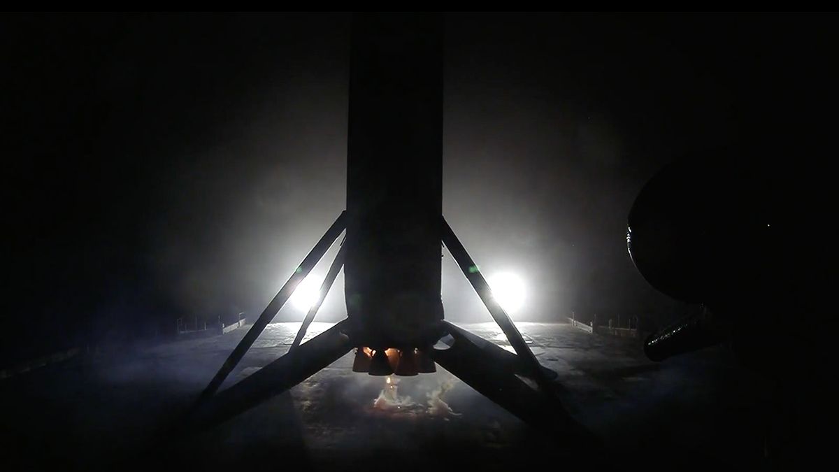 The first stage of a rocket is seen in the silhouette, backlit by lights on a sea -based droneship