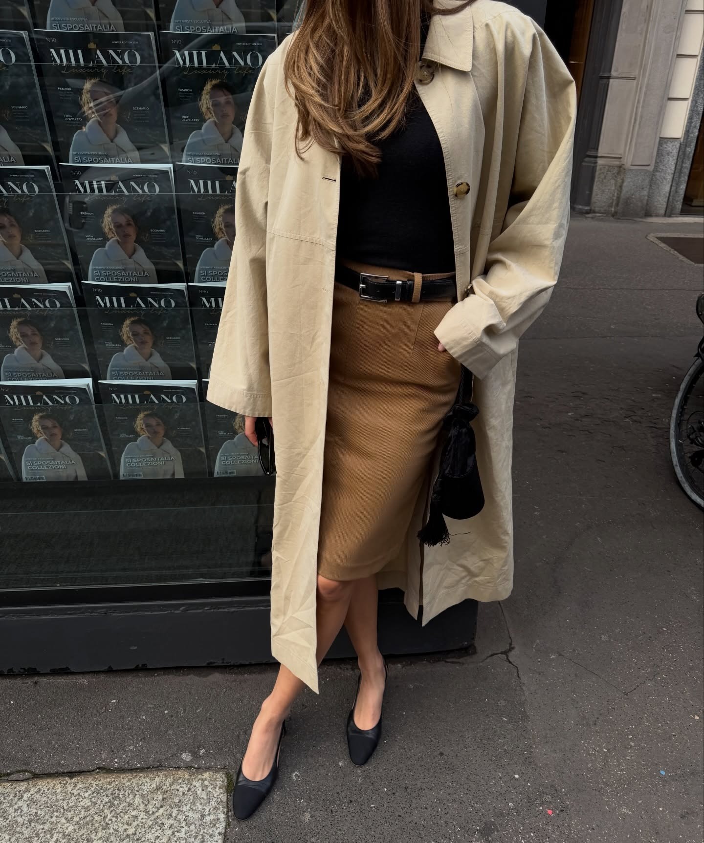 Woman in a trench, top, and belted skirt.