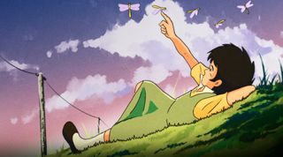 a young boy lays on a grass hill reaching up at dragonflies