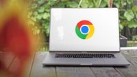 A photo of the Google Chrome logo on a white background, displayed on the screen of a large MacBook Pro which is situated on a table with green foliage behind.