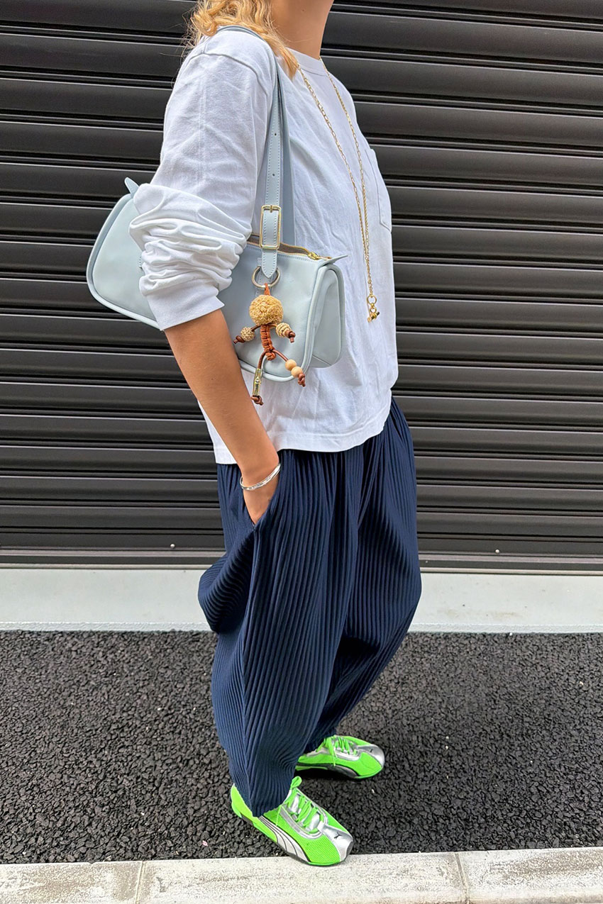 a woman wearing a white longsleeve, plisse navy pants, and green sneakers