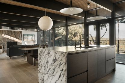 An open plan kitchen diner with a marble island, a large lamp shade, and a dark wooden dining bench 
