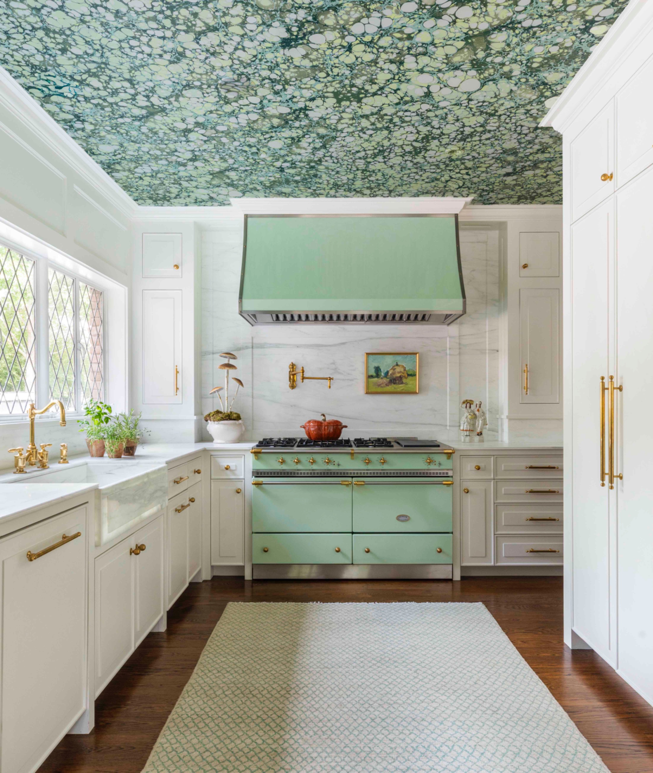 White kitchen with mint-green range and hood beneath a densely patterned green wallpapered ceiling.