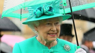 The Queen wearing a green dress and holding a green-rimmed umbrella to shelter from the rain