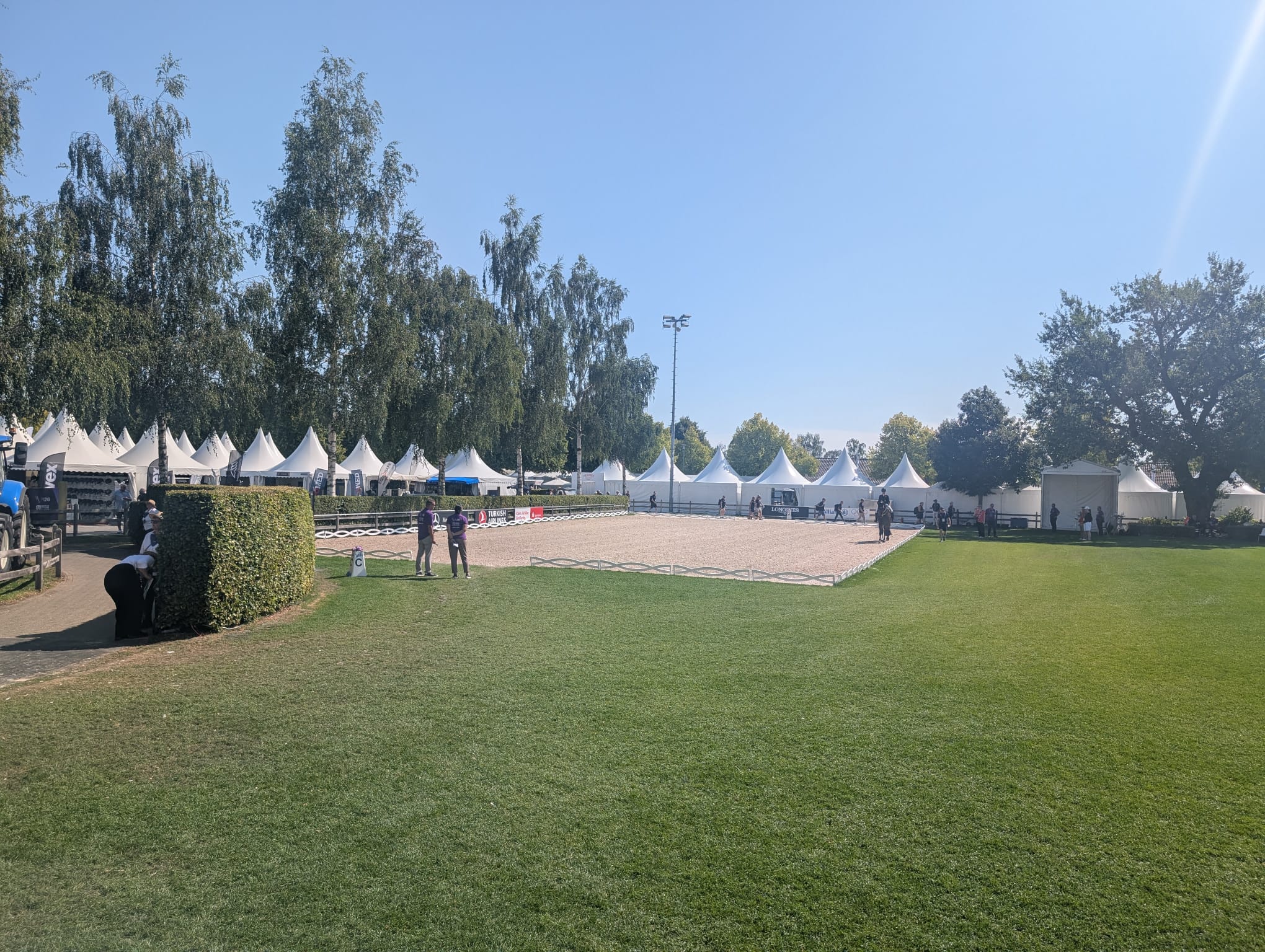 Image shows a sand dressage arena, flanked by grass and white tents