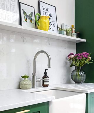 A contemporary kitchen with green cabinetry, stainless steel faucet and framed art on shelves