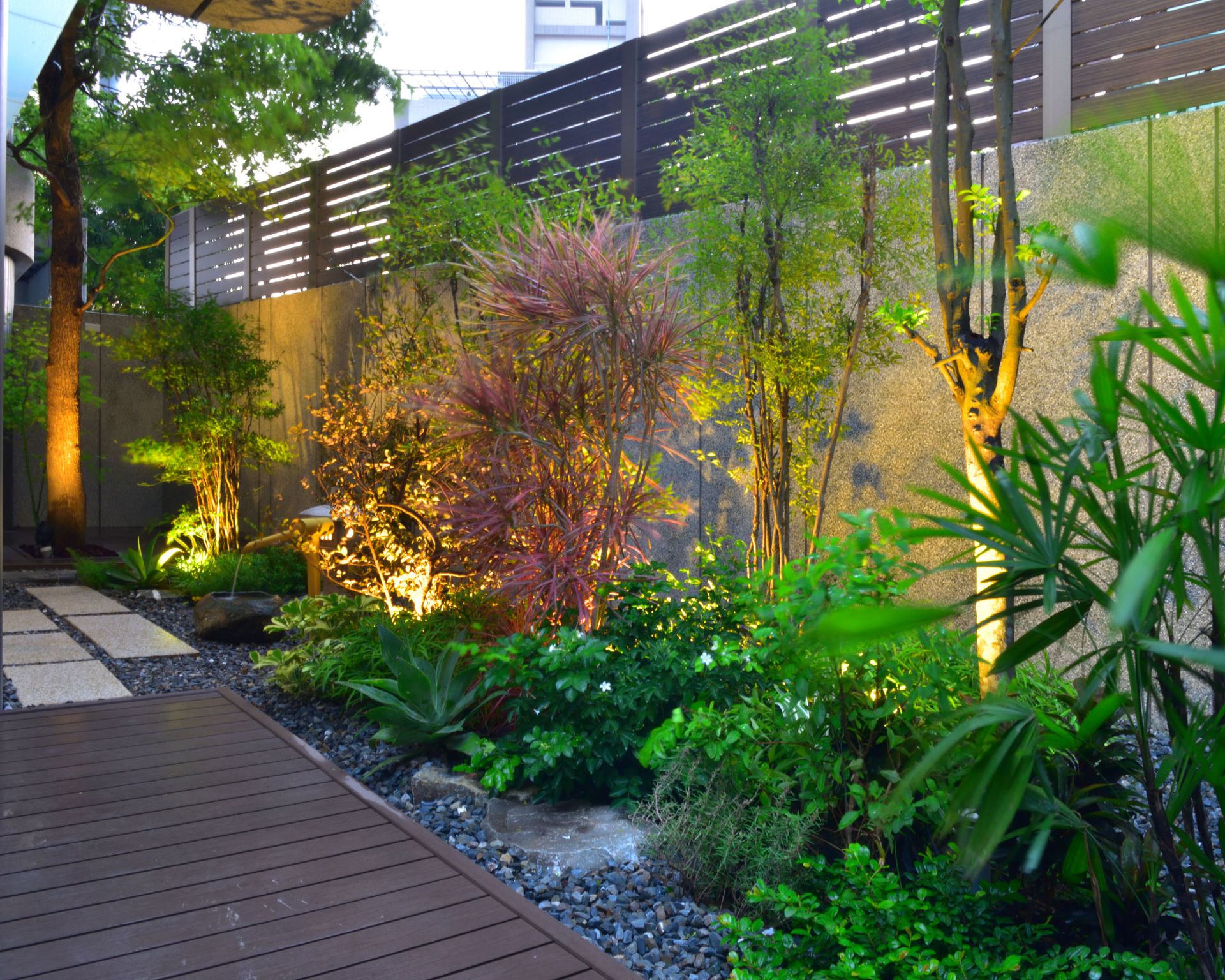 urban garden design with uplit shrubs and trees, gravel landscaping and decking