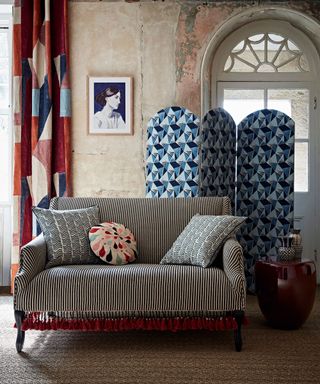 Small living room decor with compact monochrome striped sofa and a blue patterned screen, in a vintage distressed plaster scheme. behind