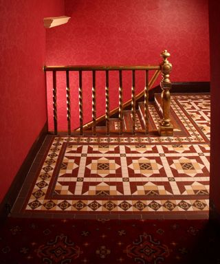 Luxurious, Victorian tile flooring in landing space in red, cream and brown colors, bright red wallpaper, wooden hand-rail
