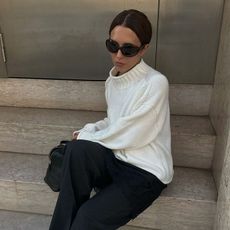 a woman wearing a cream sweater, black pants, and black heels