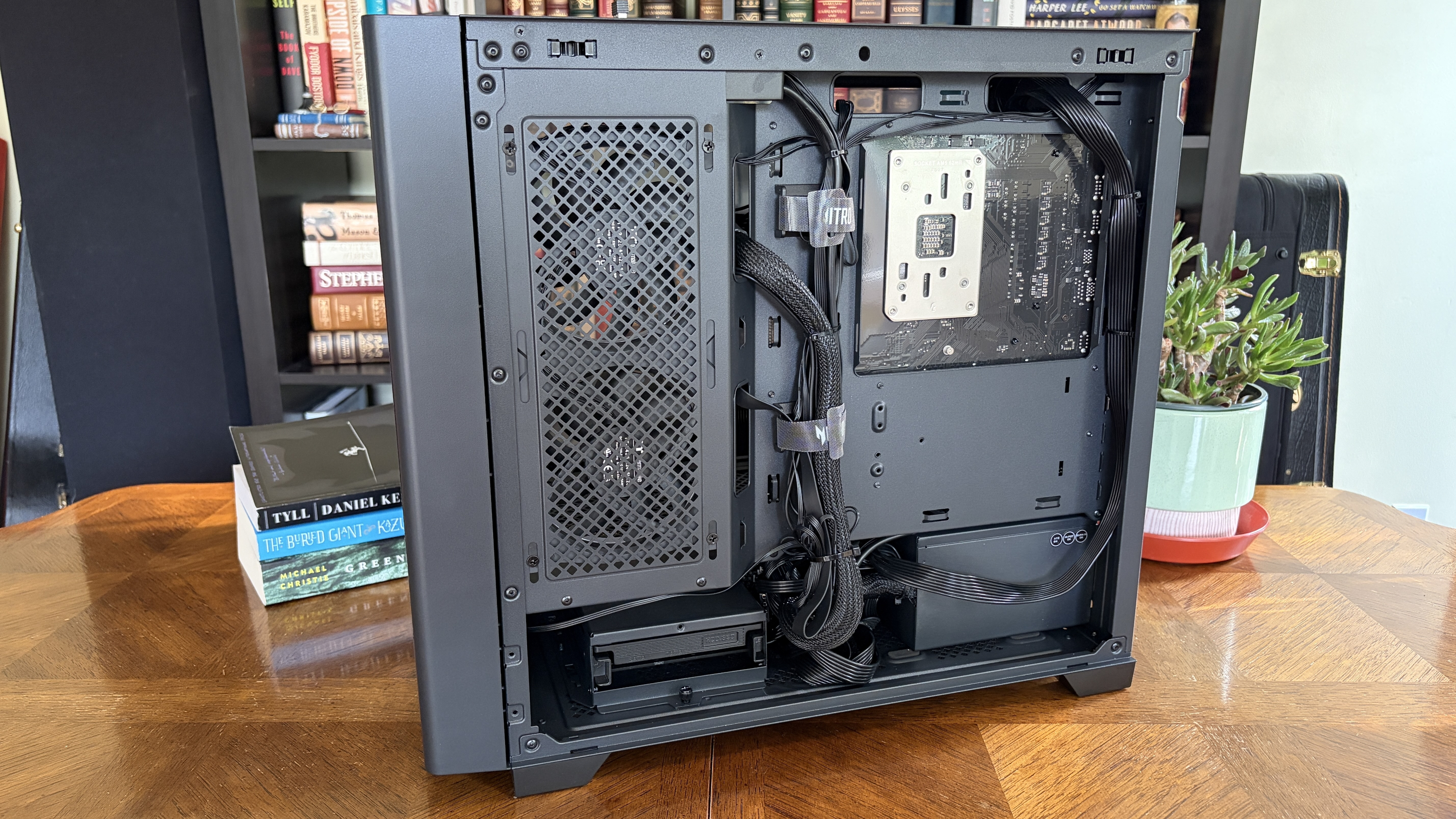 Back view of a matte black Nitro 65 computer case revealing organized internal components, including a motherboard and cables, with a bookshelf in the background.