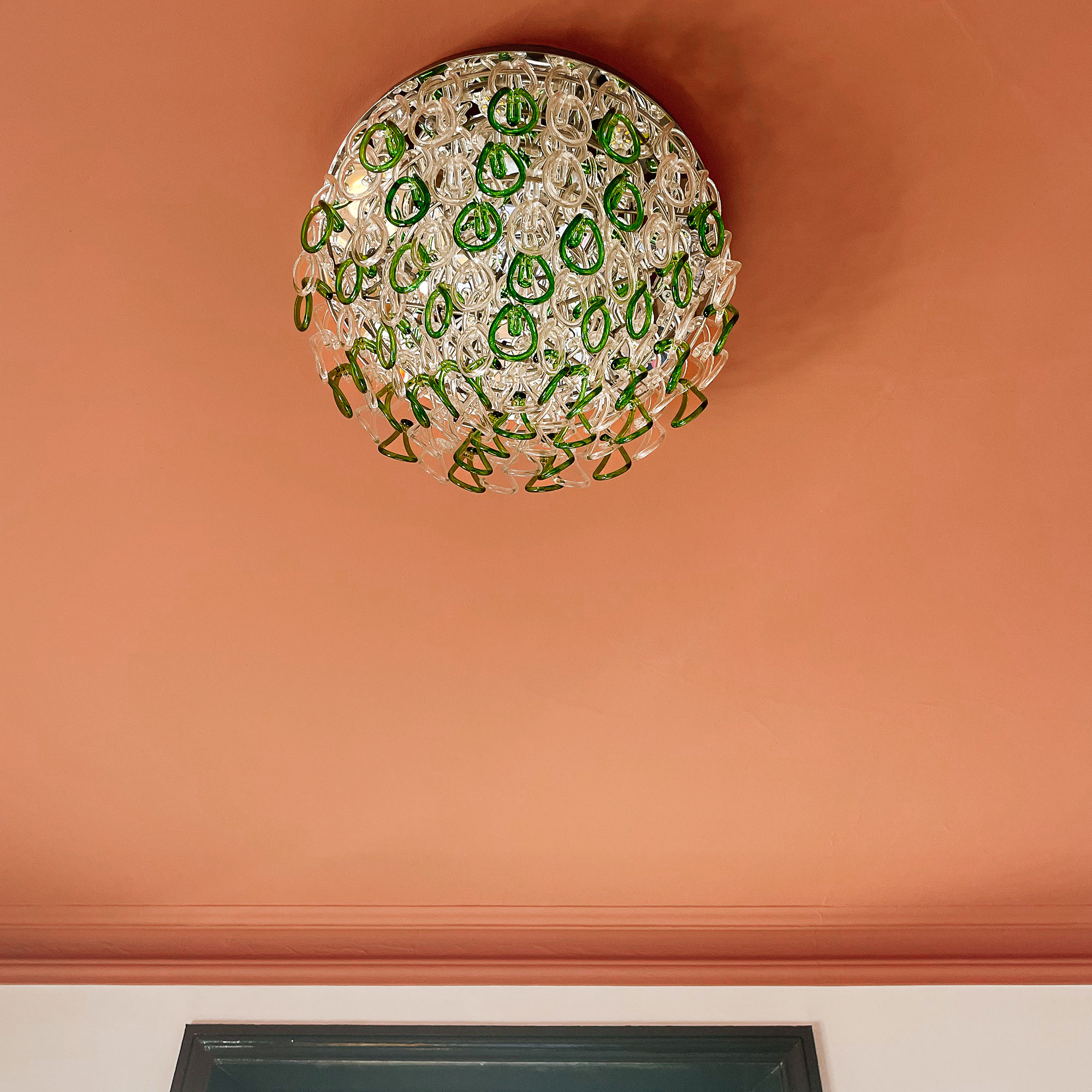 Close up of green and transparent glass chandelier on terracotta painted ceiling
