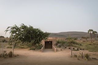 minimalist spiritual enclosure structure in pink hue concrete among desert green nature