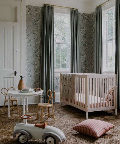 kid's bedroom with cot in one corner, toys on the floor and floral wallpaper on the walls