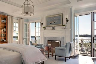bedroom with french windows open to balcony and ocean view with blue armchairs around fireplace and white bedding