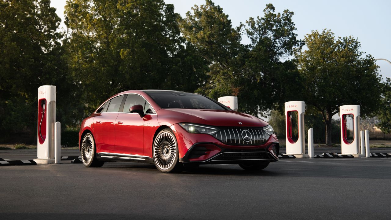 A red Mercedes EV parked in front of a bay of Tesla chargers