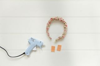 A glue gun on a table next to a fabric hairband.