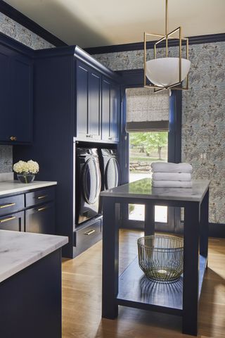 dark blue laundry room with wooden floors, wallpaper, blind on door, island, pendant, washers, countertops