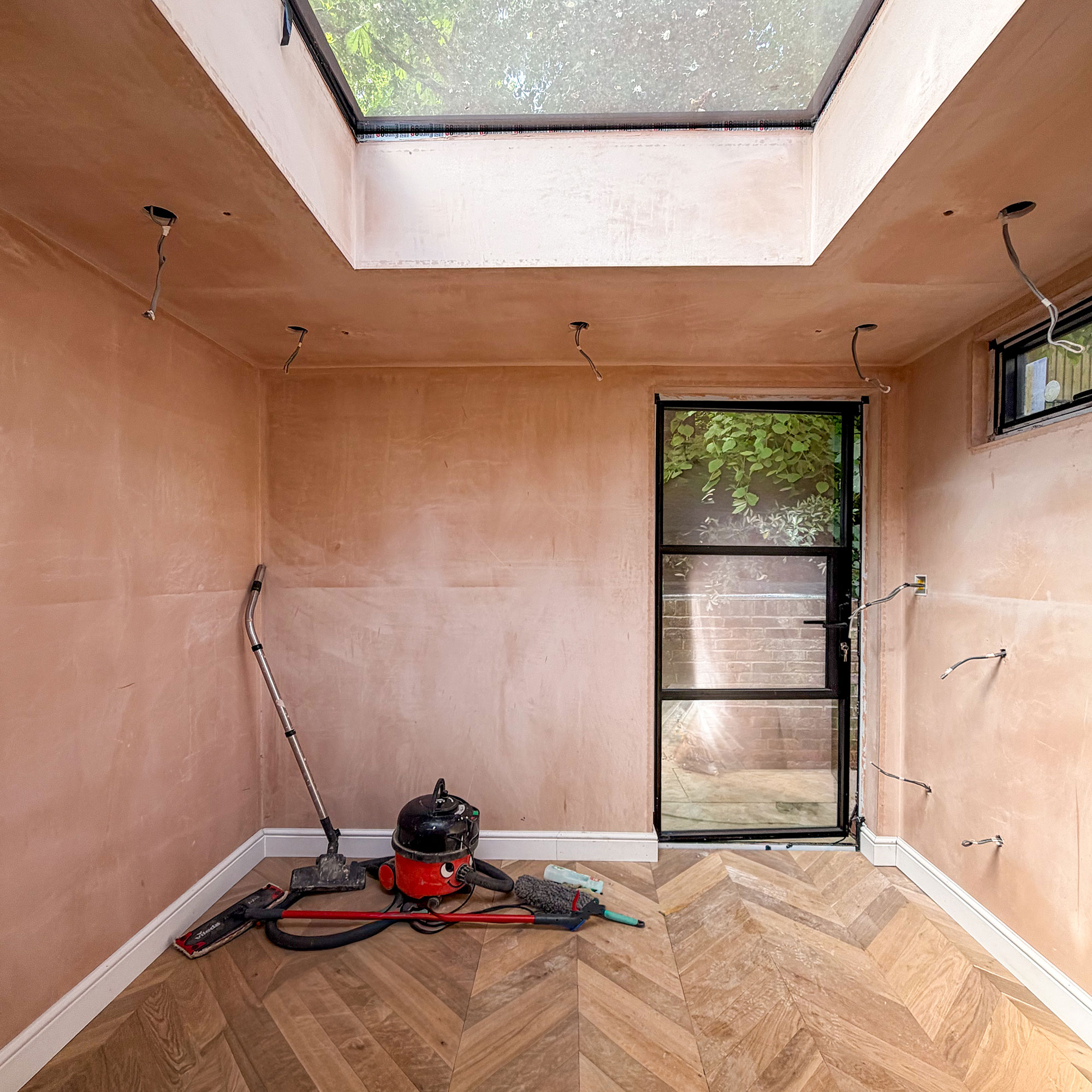 Empty room mid renovation with plaster walls, wooden parquet, rooflight and Henry Hoover