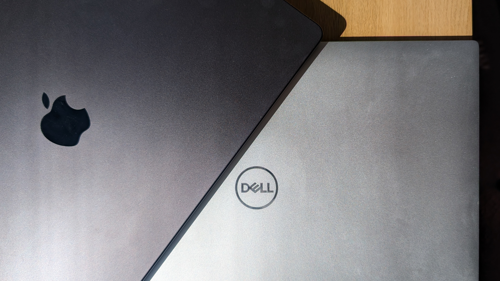 A MacBook Pro positioned on top of a Dell XPS, lit by the sun.