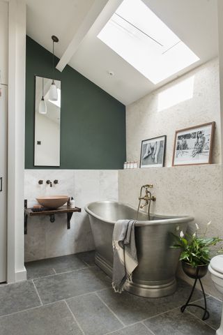 rustic bathroom with brushed steel roll top bath, tiled floor, stone slab walls, wall mounted basin, green painted wall loft
