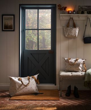 An entryway with a dark blue door, white wooden paneled walls, wooden flooring, and bags around it