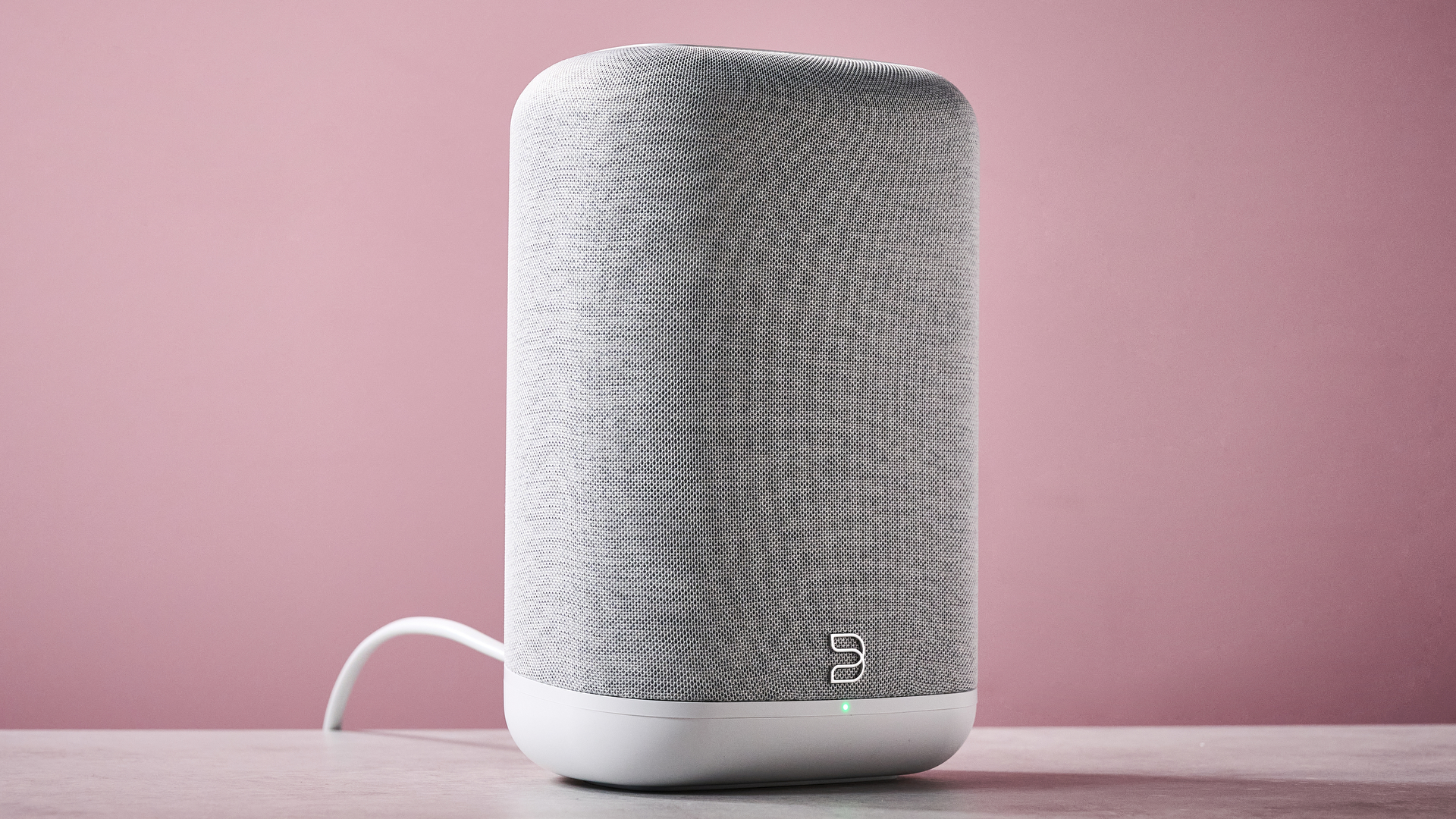 The Bluesound Pulse Flex at a 3/4 angle on a stone effect counter in front of a pink background.