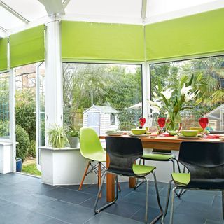 A conservatory with lime green blinds and a wooden dining table with green chairs