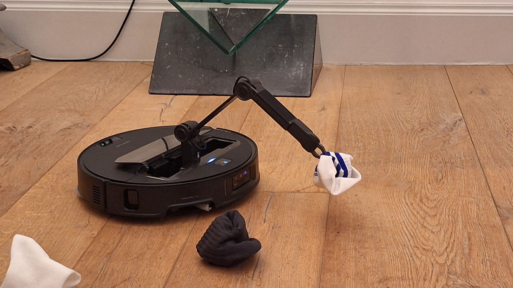 Roborock Saros Z70 robot vacuum picking up a sock with its pincer arm