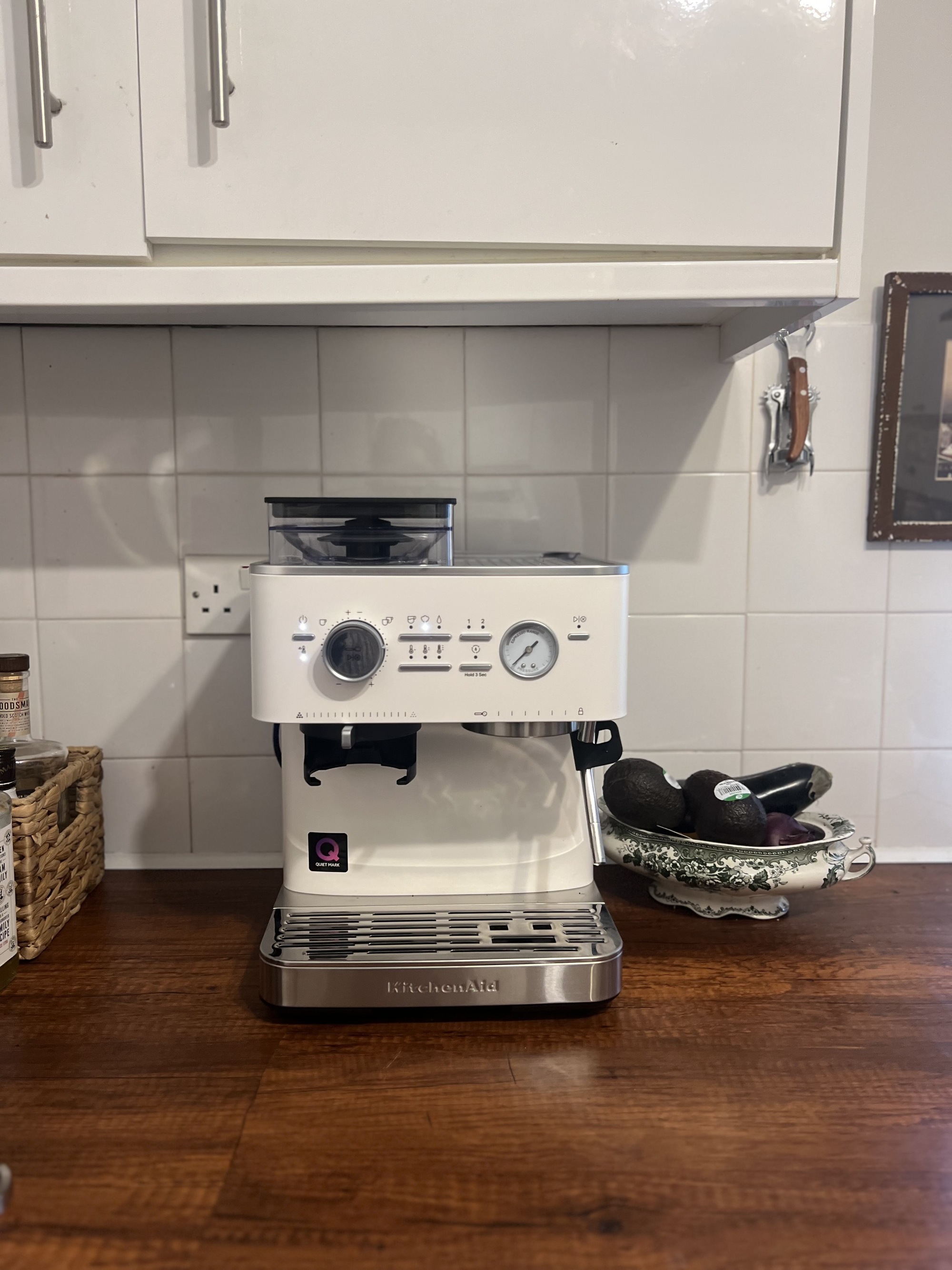 Image of a white KitchenAid coffee machine on a wooden countertop with a white tile backsplash and white cabinetry above the machine