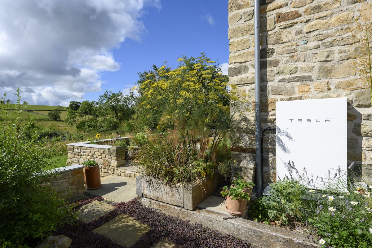 stone barn with tesla powerwall on exterior wall with view of garden