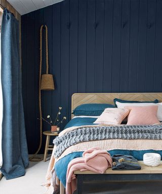 Bedroom with navy blue wooden wall panelling behind bed
