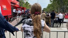 A girl stands at the barrier at a Grand Tour cycle race watching a team time trial about to start