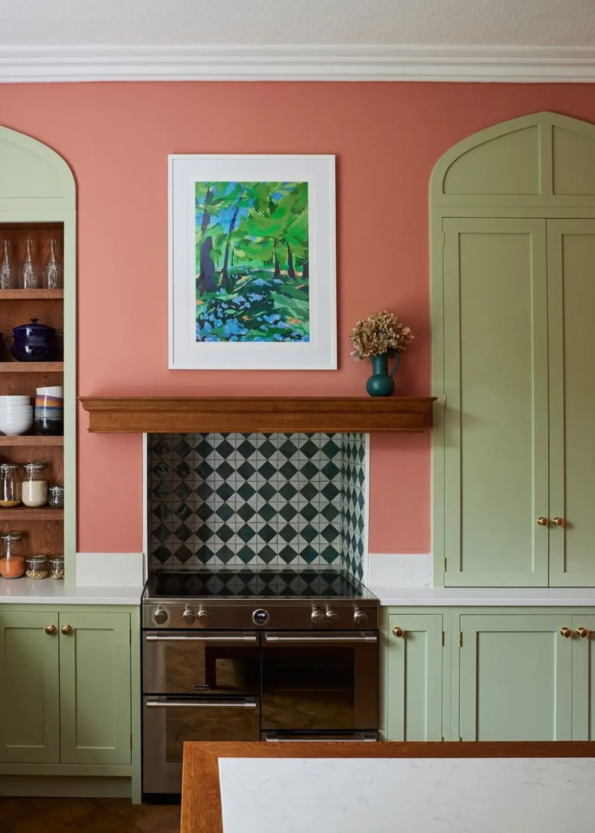 A kitchen with peach walls and light green cabinets, and a tiled oven backsplash.