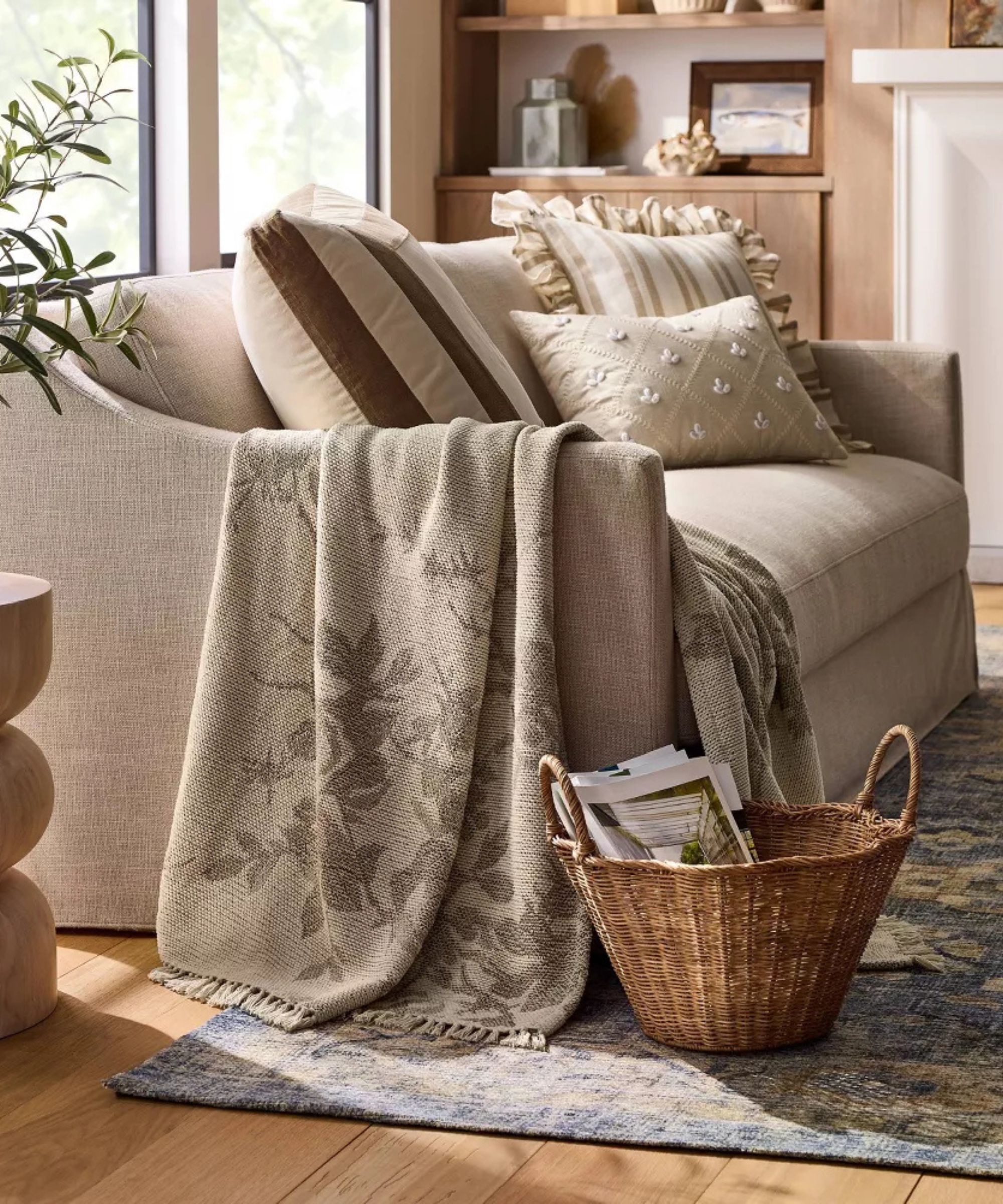 A neutral loveseat sofa adorned with a mix of warm neutral patterned pillows and a floral throw blanket over the arm