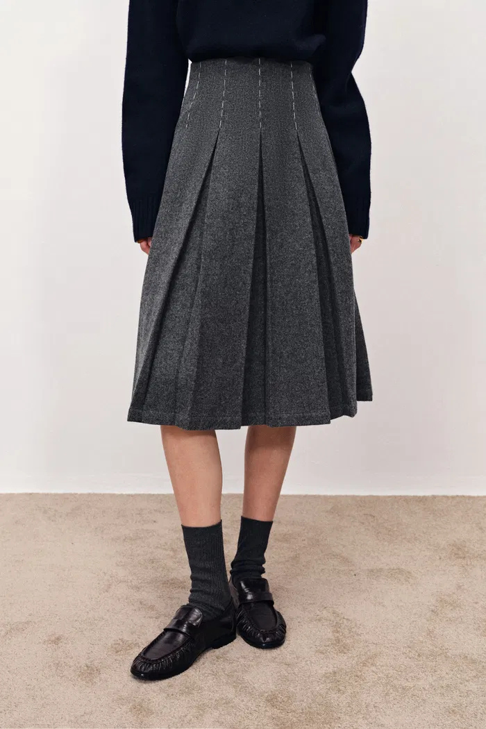 A women wearing a grey pleated skirt.