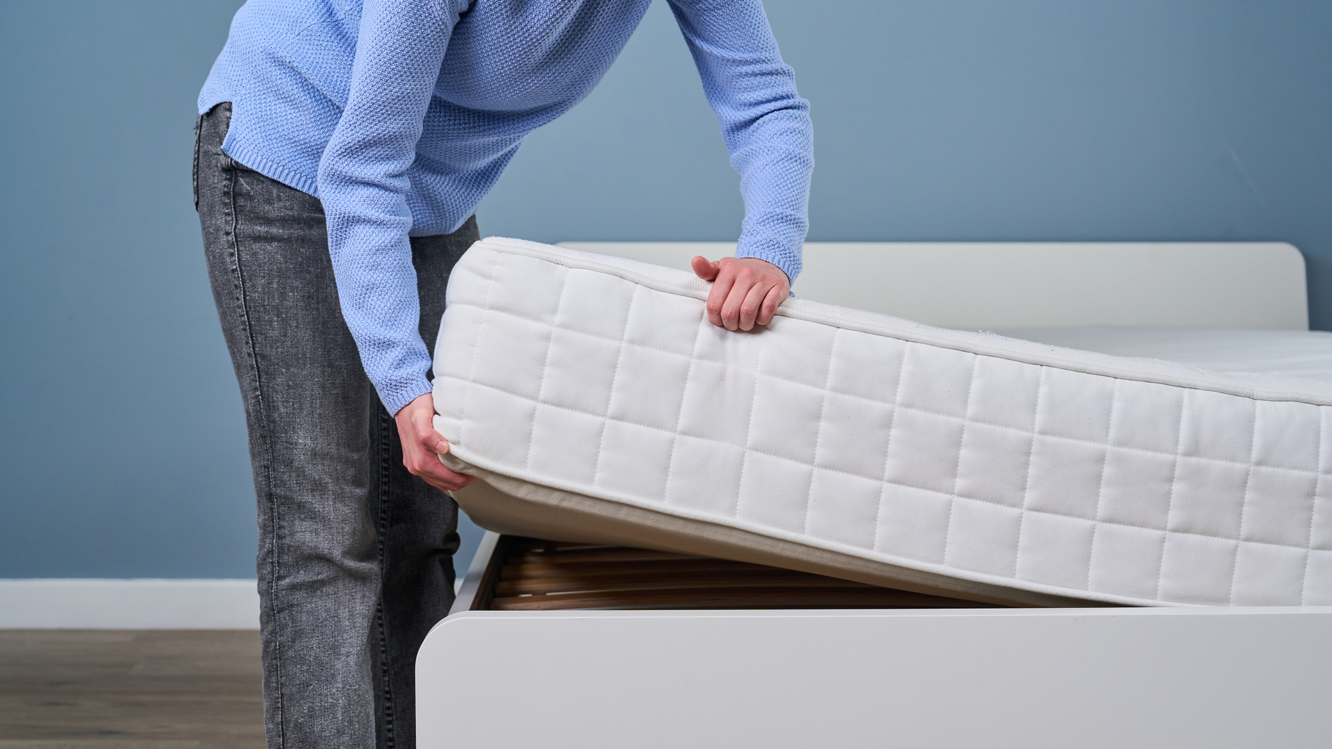 A woman's hand lift the corner of an innerspring mattress.