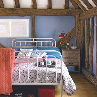 bedroom with blue wall wooden beams white bed with designed cushions and wooden floor