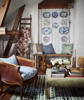 make your home feel like a sanctuary, cottage style living room with plates on wall, rattan armchair with blue cushion, green velvet footstool, ladder, log store