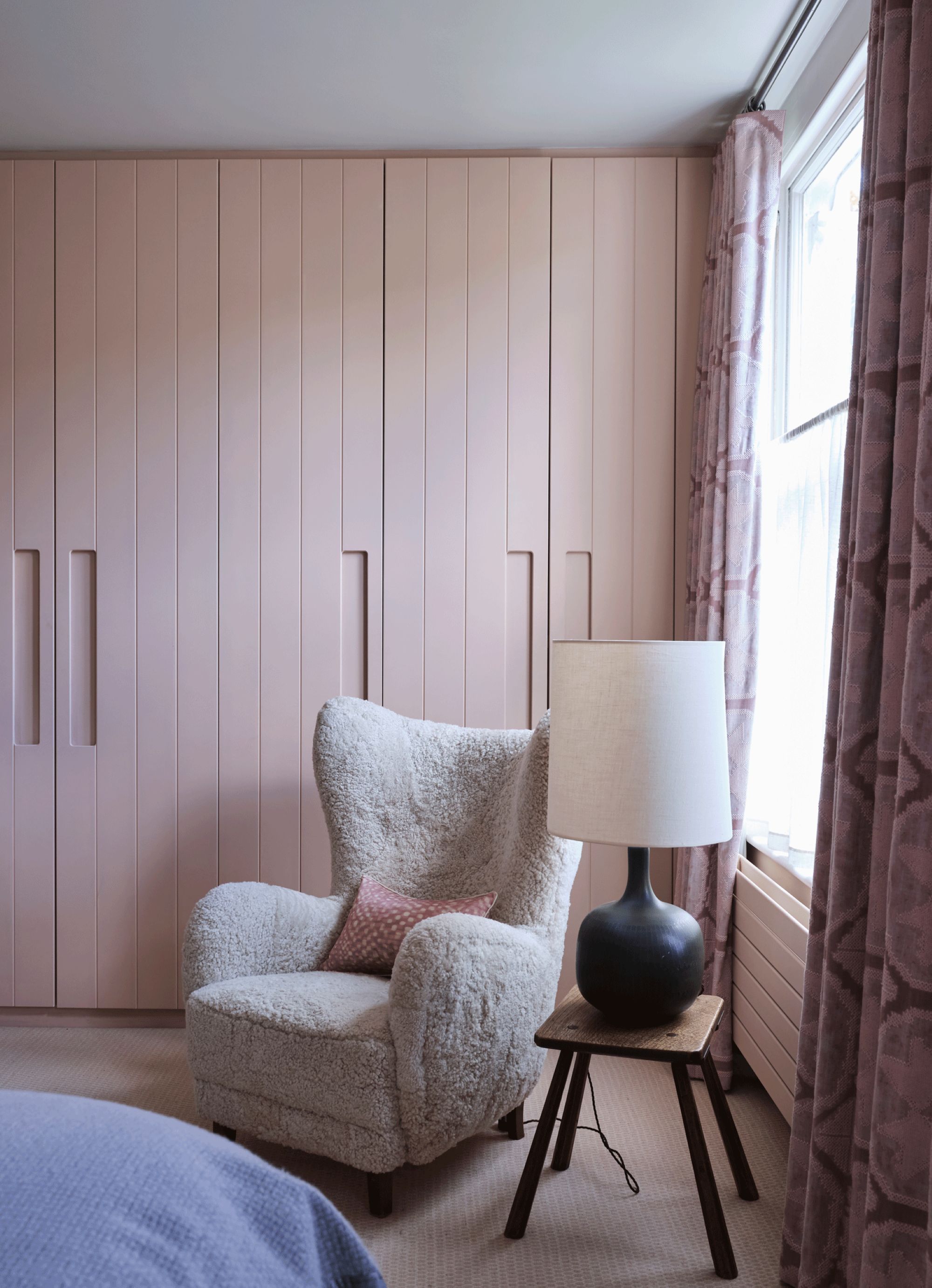 teddy armchair reading corner sitting in front of a wall of pink closets and next to a small end table holding a black table lamp