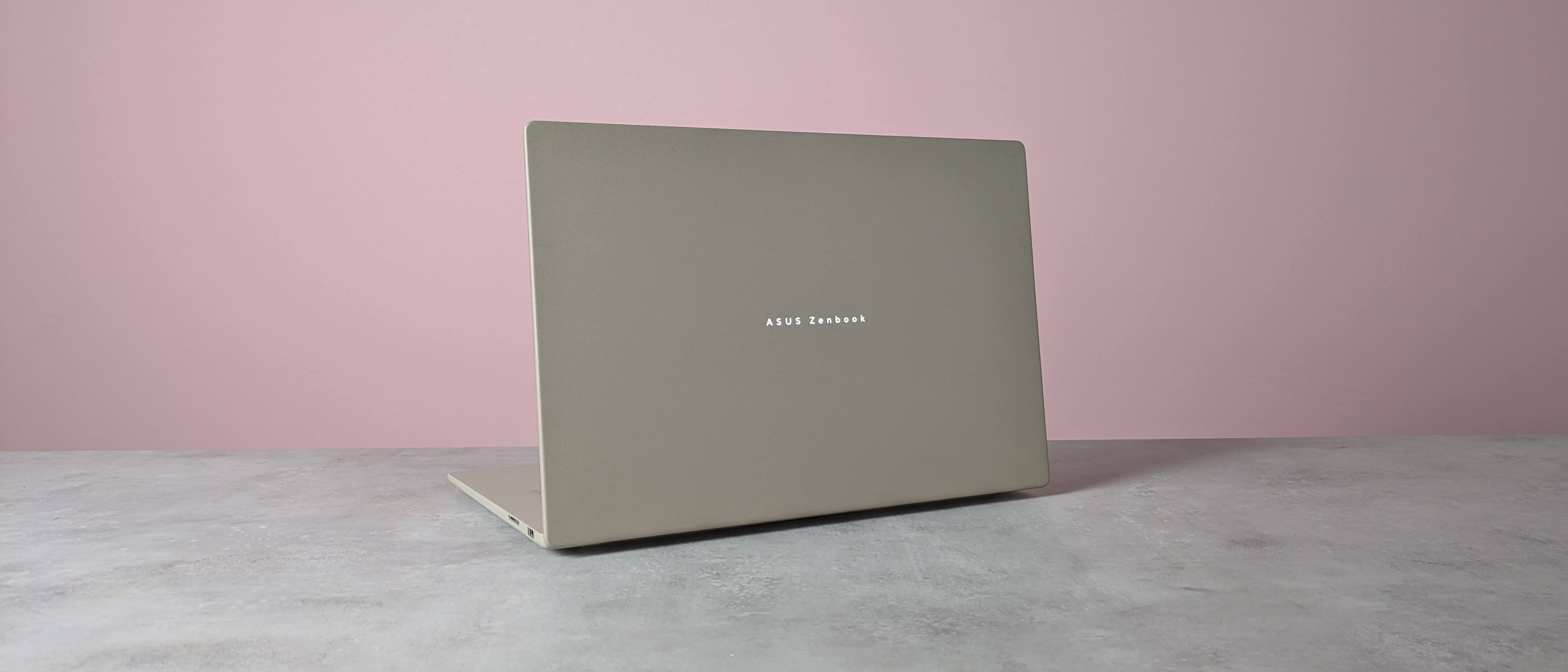 Rear three-quarter view of Asus Zenbook A16 open on desk with pink wall in background