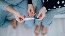 A couple hold a hands and a pregnancy test together.